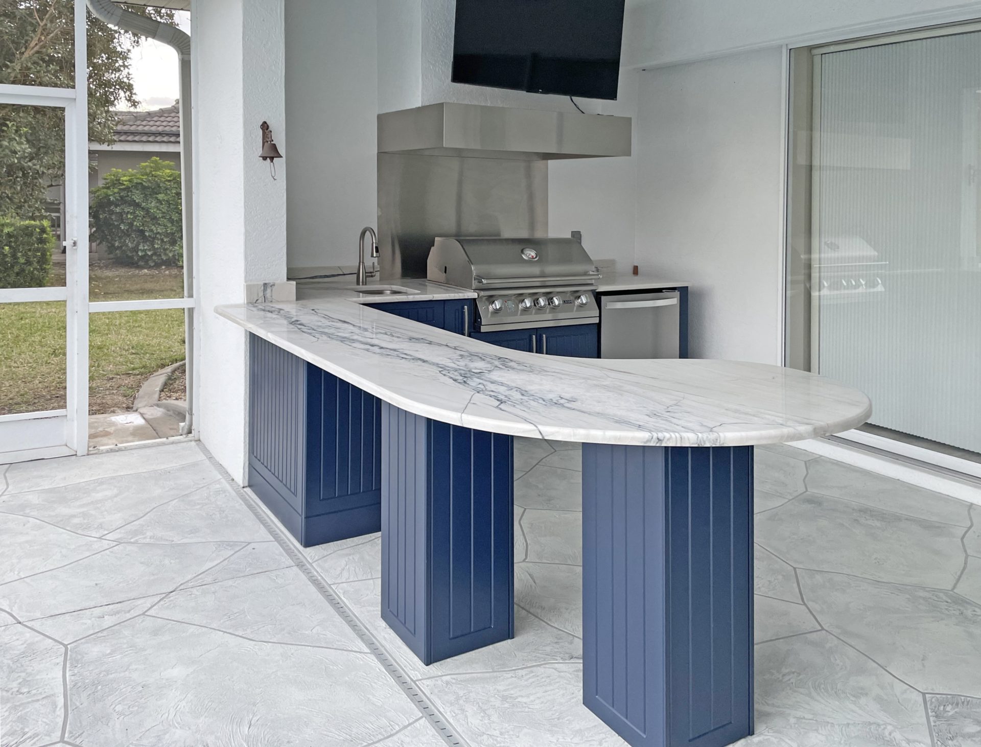 OUTDOOR KITCHEN 20. Custom outdoor kitchen in Lakewood Ranch, FL. Kitchen features blue, v-groove style doors. Appliances include Lion grill, Falmec outdoor hood, stucco hood chase w/TV, Bull stainless front refrigerator and stainless bar pulls.