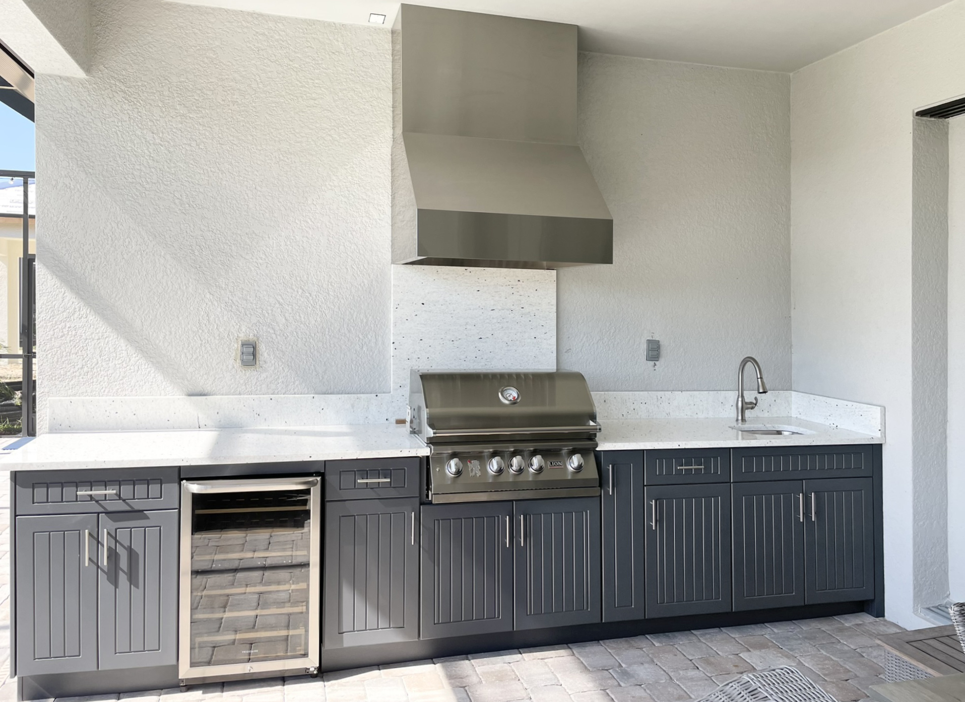 OUTDOOR KITCHEN 25. Custom outdoor kitchen in Lakewood Ranch, FL. Kitchen features charcoal grey, v-groove style cabinets. Appliances include Lion grill, Tradewind outdoor hood, stainless hood chase, Azure glass front refrigerator and stainless bar pulls.
