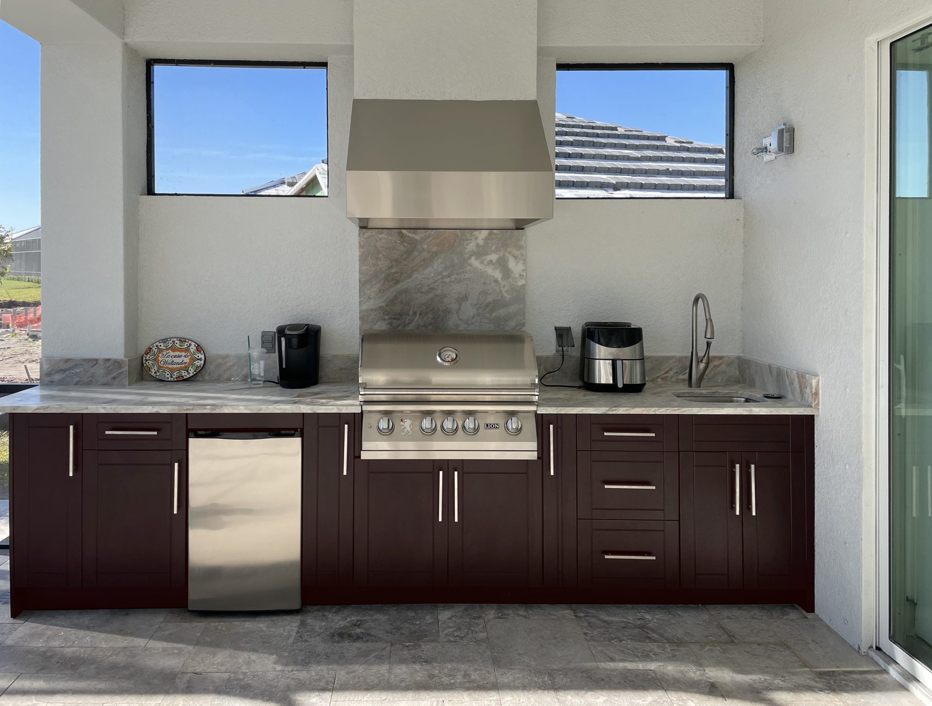 OUTDOOR KITCHEN 33. Custom outdoor kitchen in Lakewood Ranch, FL. Kitchen features dark brown, shaker style cabinets. Appliances include Lion grill, Tradewind outdoor hood, stucco hood chase and Blaze stainless front refrigerator & bar pulls.