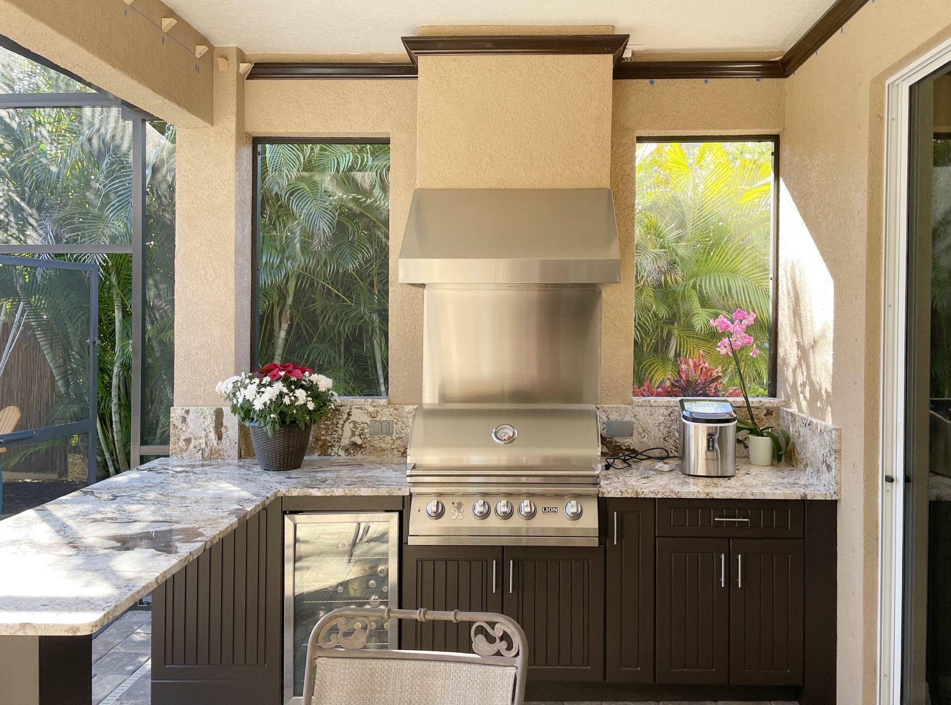 OUTDOOR KITCHEN 34. Custom outdoor kitchen in Parris, FL. Kitchen features dark brown, v-groove style cabinets. Appliances include Lion grill, Cypress outdoor hood, stucco hood chase, glass front refrigerator and stainless backsplash & bar pulls.