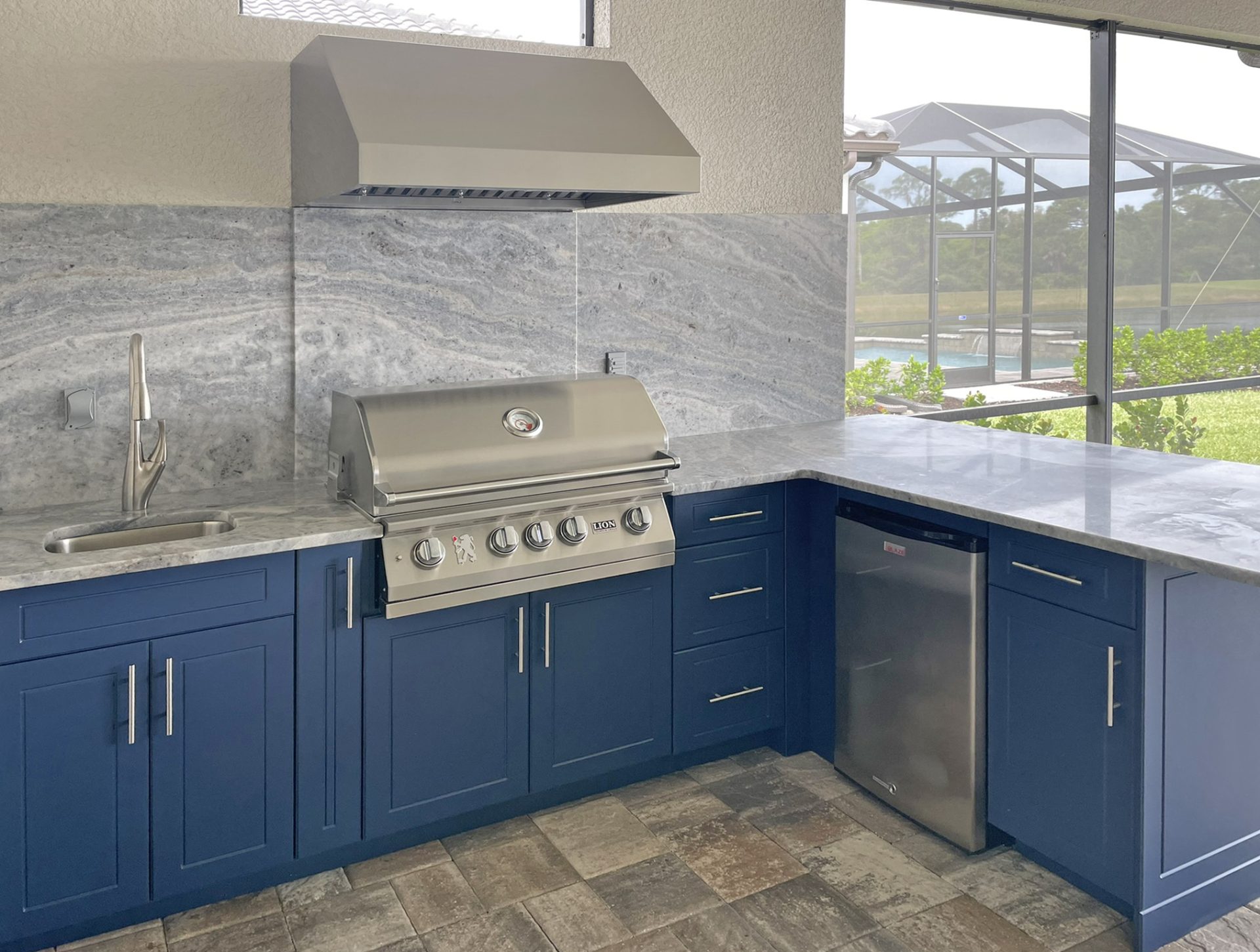 OUTDOOR KITCHEN 35. Custom outdoor kitchen in Lakewood Ranch, FL. Kitchen features indigo blue, v-groove style cabinets. Appliances include Lion grill, Cypress outdoor hood, Blaze stainless front refrigerator and stainless bar pulls.
