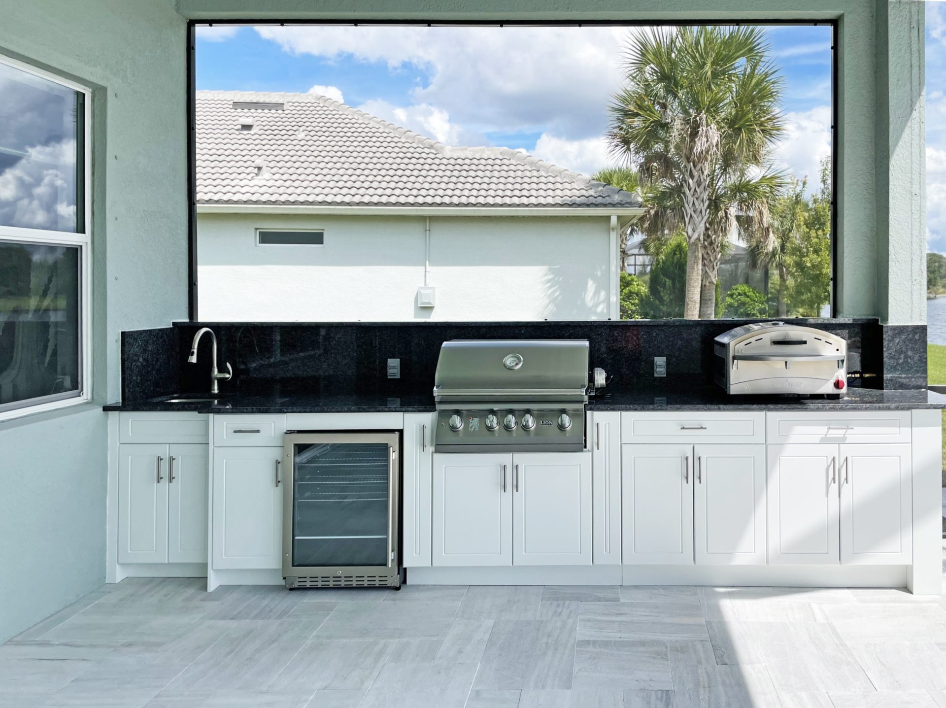 OUTDOOR KITCHEN 39. Custom outdoor kitchen in Venice, FL. Kitchen features white, sport style cabinets. Appliances include Lion grill, Camp Chef pizza oven, glass front refrigerator and stainless bar pulls.