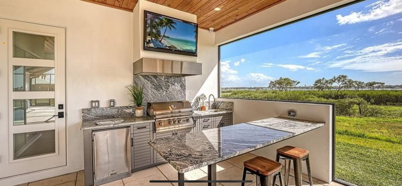 OUTDOOR KITCHEN 42. Custom outdoor kitchen in Palmetto, FL. Kitchen features stainless, cabana style cabinets. Appliances include Lion grill, Heat Versa outdoor hood, stucco hood chase w/TV, Blaze stainless front refrigerator and black bar pulls.