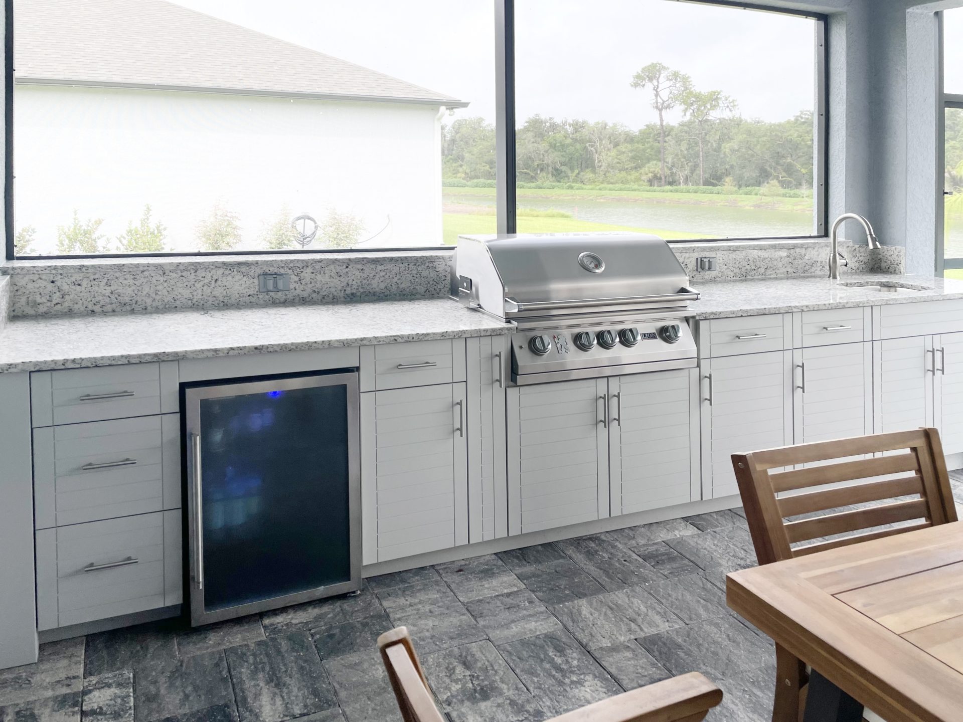 OUTDOOR KITCHEN 5. Custom outdoor kitchen in Parrish, FL. Kitchen features dolphin grey, cabana style cabinets. Appliances include Lion grill, glass front refrigerator and stainless bar pulls.