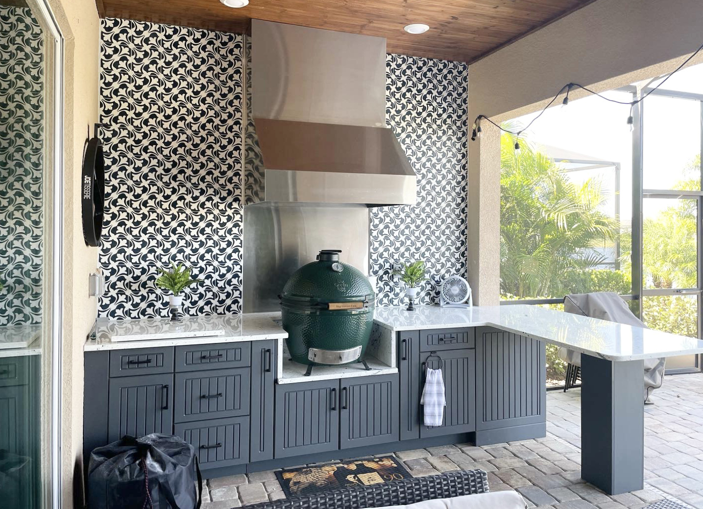OUTDOOR KITCHEN 6. Custom outdoor kitchen in Lakewood Ranch, FL. Kitchen features charcoal grey, v-groove style cabinets. Appliances include Big Green Egg, Tradewind hood, stainless hood chase, stainless backsplash and black bar pulls.