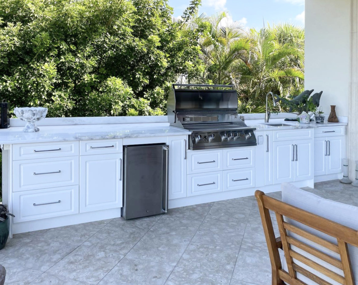 OUTDOOR KITCHEN 7. Custom outdoor kitchen in Casey Key, FL. Kitchen features white, coastal style cabinets. Appliances include Lion grill, stainless front refrigerator and stainless bar pulls.