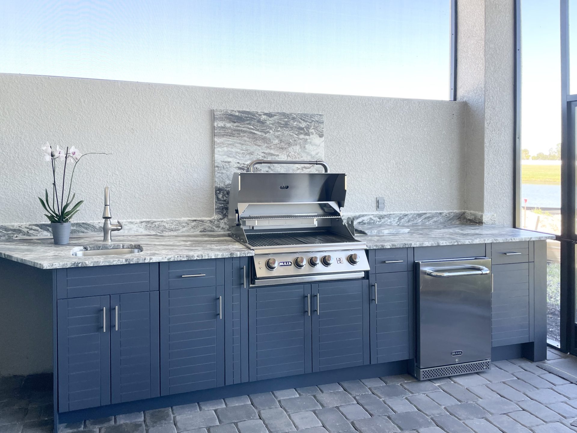 OUTDOOR KITCHEN 8. Custom outdoor kitchen in Palmetto, FL. Kitchen features charcoal grey, cabana style cabinets. Appliances include Bull grill, Bull stainless refrigerator and stainless bar pulls.